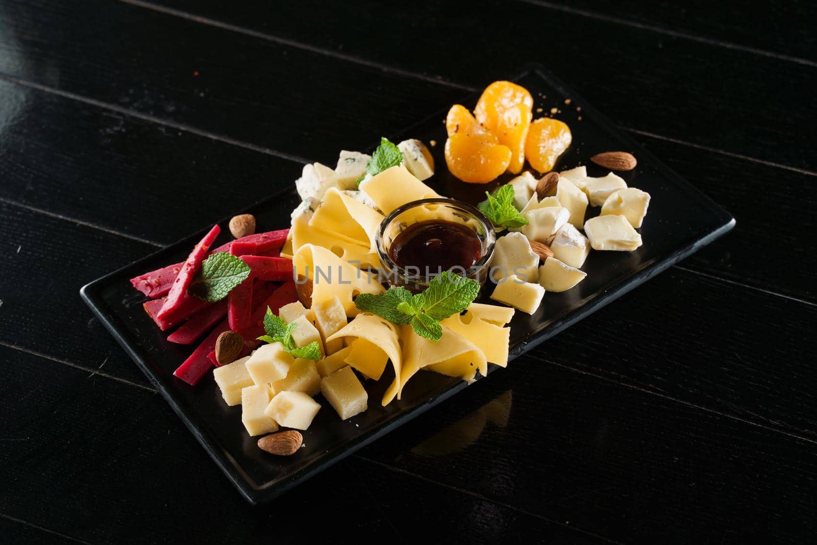 Cheese food board with delicous cheeses, walnuts. Parmesan, jam, dorblu on the black plate. Food appetizer from restaurant