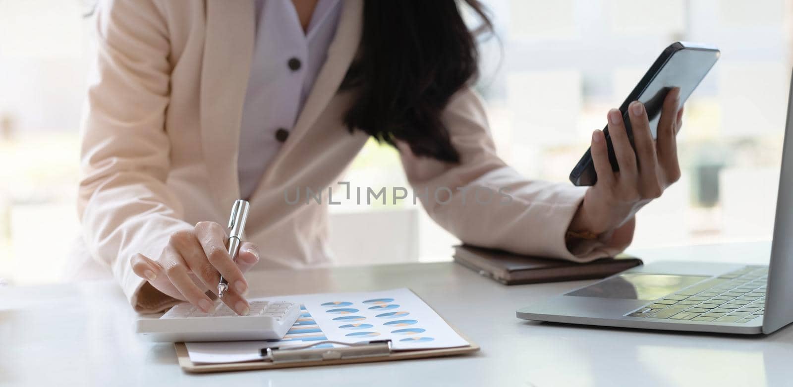 Close-up of a businesswoman hand holding a pen and smartphone using a calculator to calculate statistics analysis at the office..