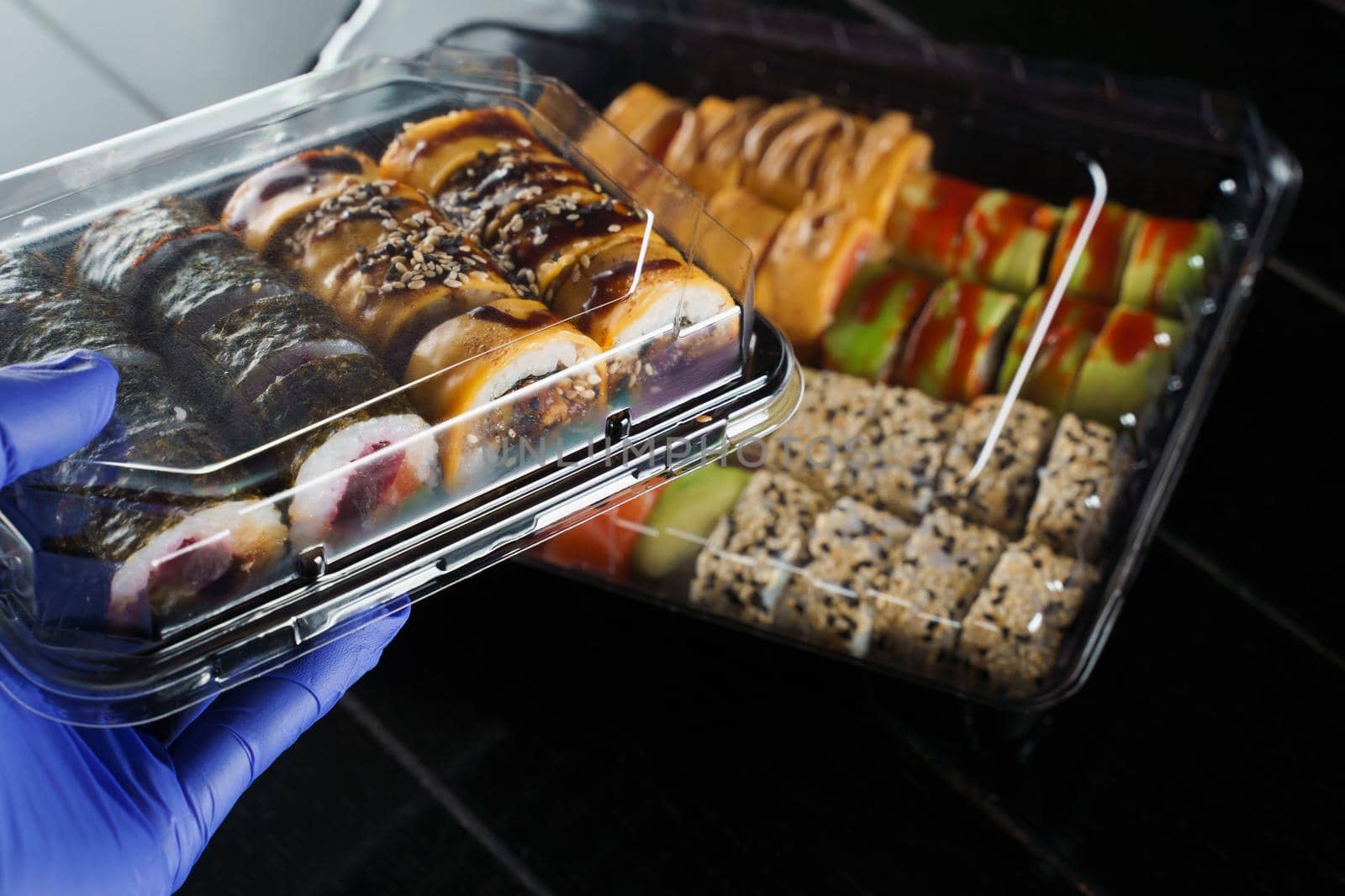 Sushi roll food delivery service at quarantine covid-19 period. Holding sushi set box using medical gloves on black background. by Rabizo