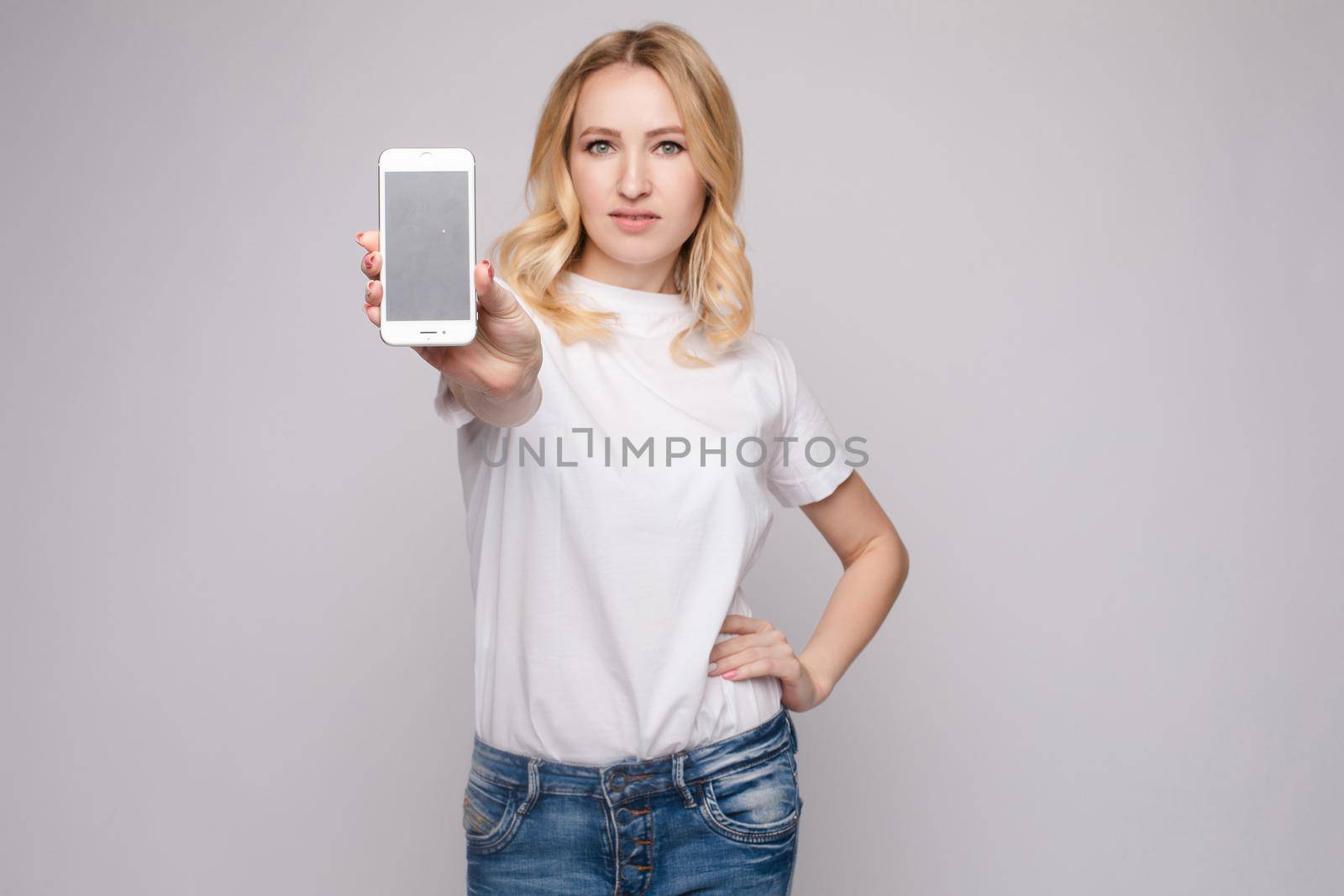 Studio portrait of beautiful caucasian brunette woman in patterned overall pointing at her smartphone with index finger. She is certain or sure about something. I know gesture.