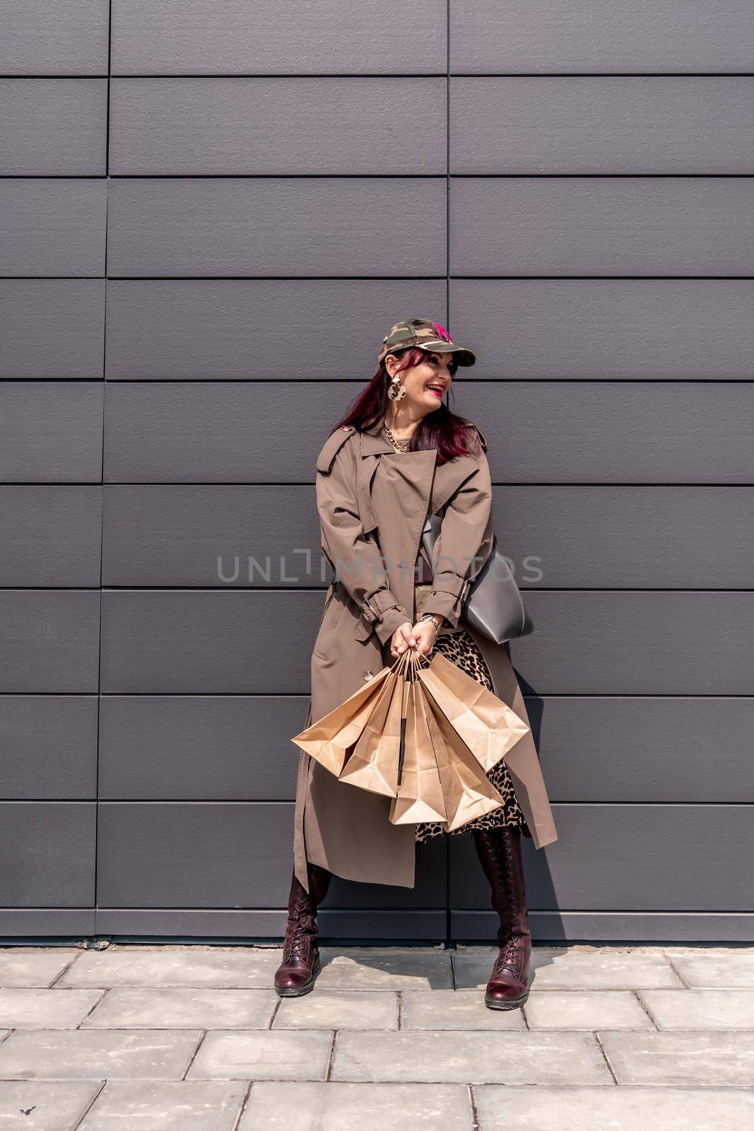 A happy shopaholic girl keeps her bags near the shopping center. A woman near the store is happy with her purchases, holding bags. Dressed in a leopard print dress. Consumer concept