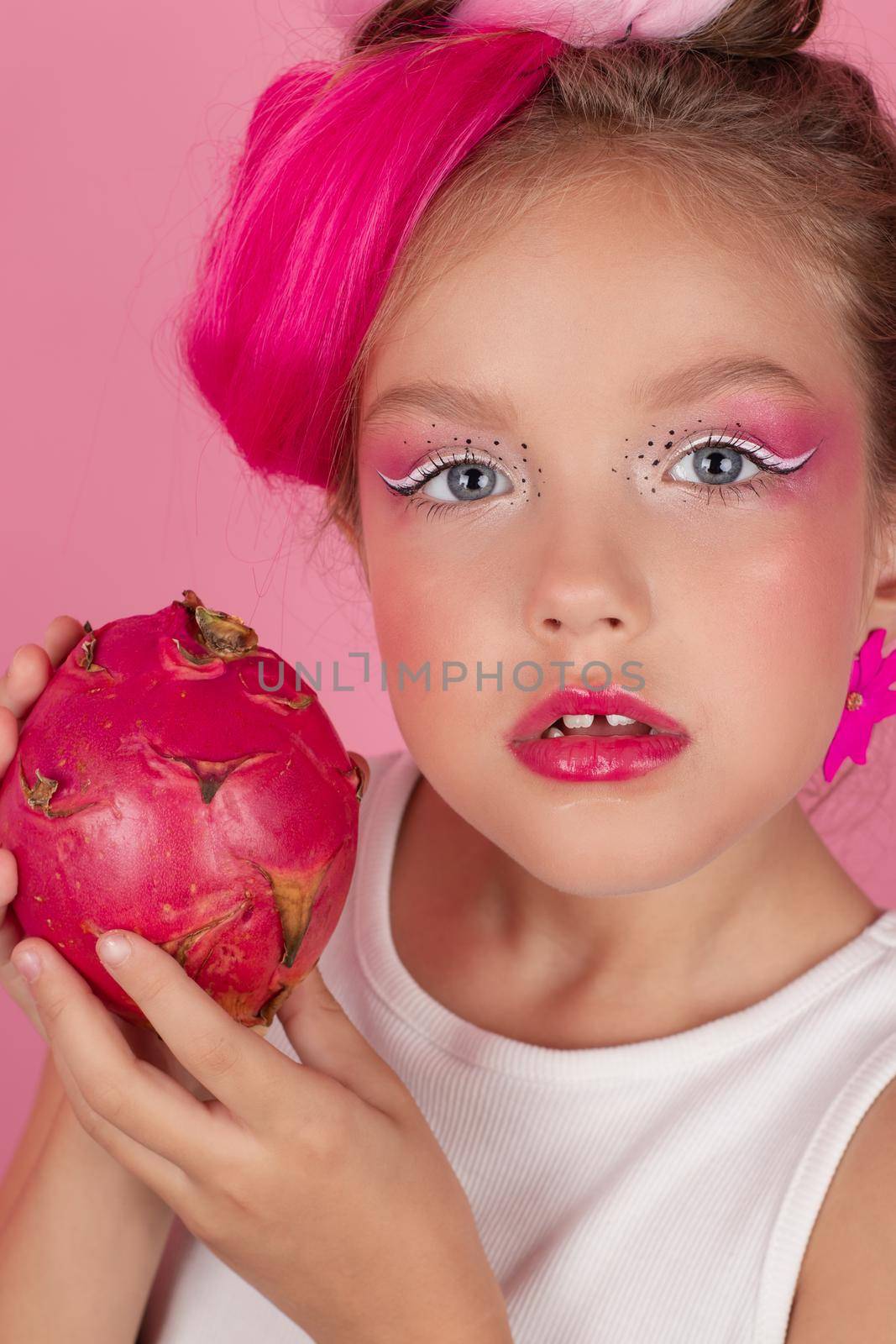 sweet Girl is holding a Pitahaya near her face. A pitaya fruit hold in hand on pink background. Tropical Dragon Fruit cut in half. space for text. by oliavesna