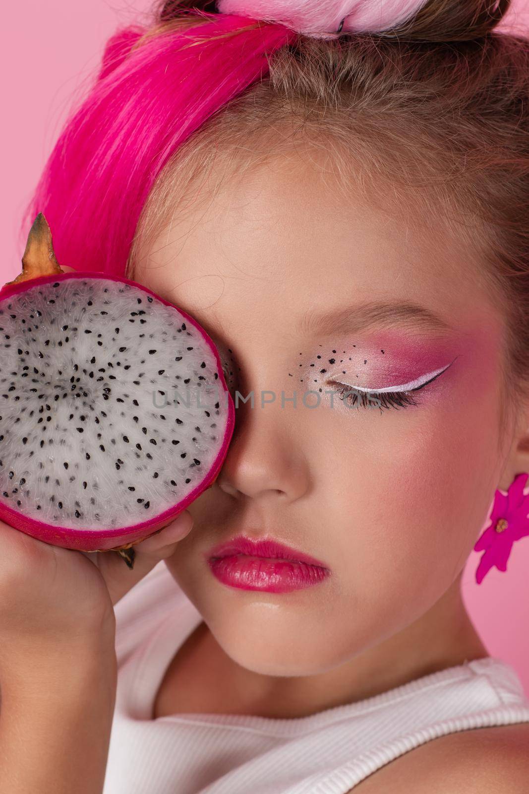 sweet Girl is holding a Pitahaya near her face. A pitaya fruit hold in hand on pink background. Tropical Dragon Fruit cut in half. space for text. by oliavesna