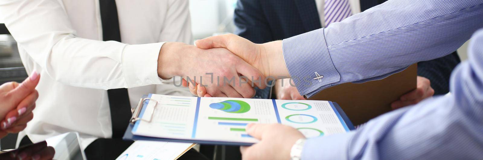 Close-up of smart colleagues smiling and shaking hand with prudent boss. Young manager giving important business project that determine future of corporation. Company meeting concept