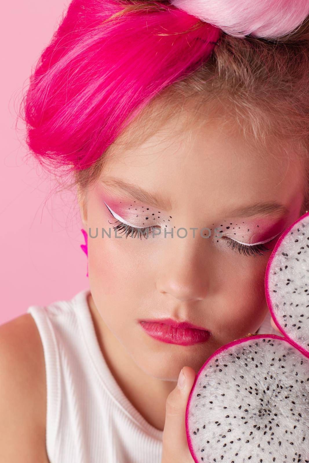 sweet Girl is holding a Pitahaya near her face. A pitaya fruit hold in hand on pink background. Tropical Dragon Fruit cut in half. space for text