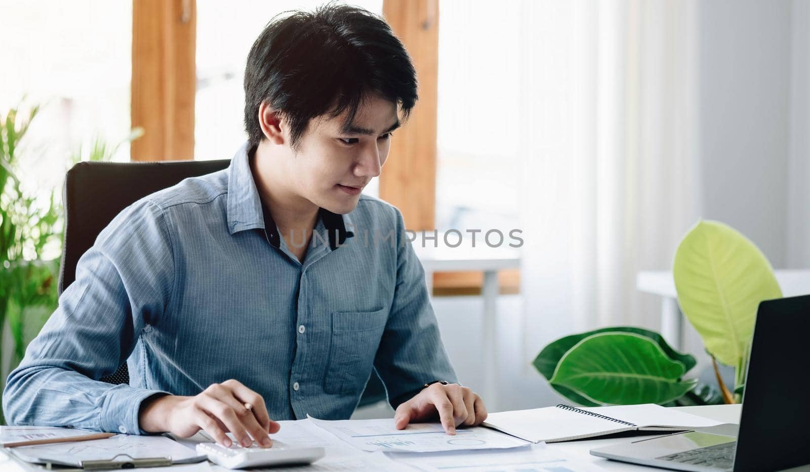 Portrait of Young Asian man hand freelancer is working her job on computer tablet in modern office. Doing accounting analysis report real estate investment data, Financial and tax systems concept. by wichayada