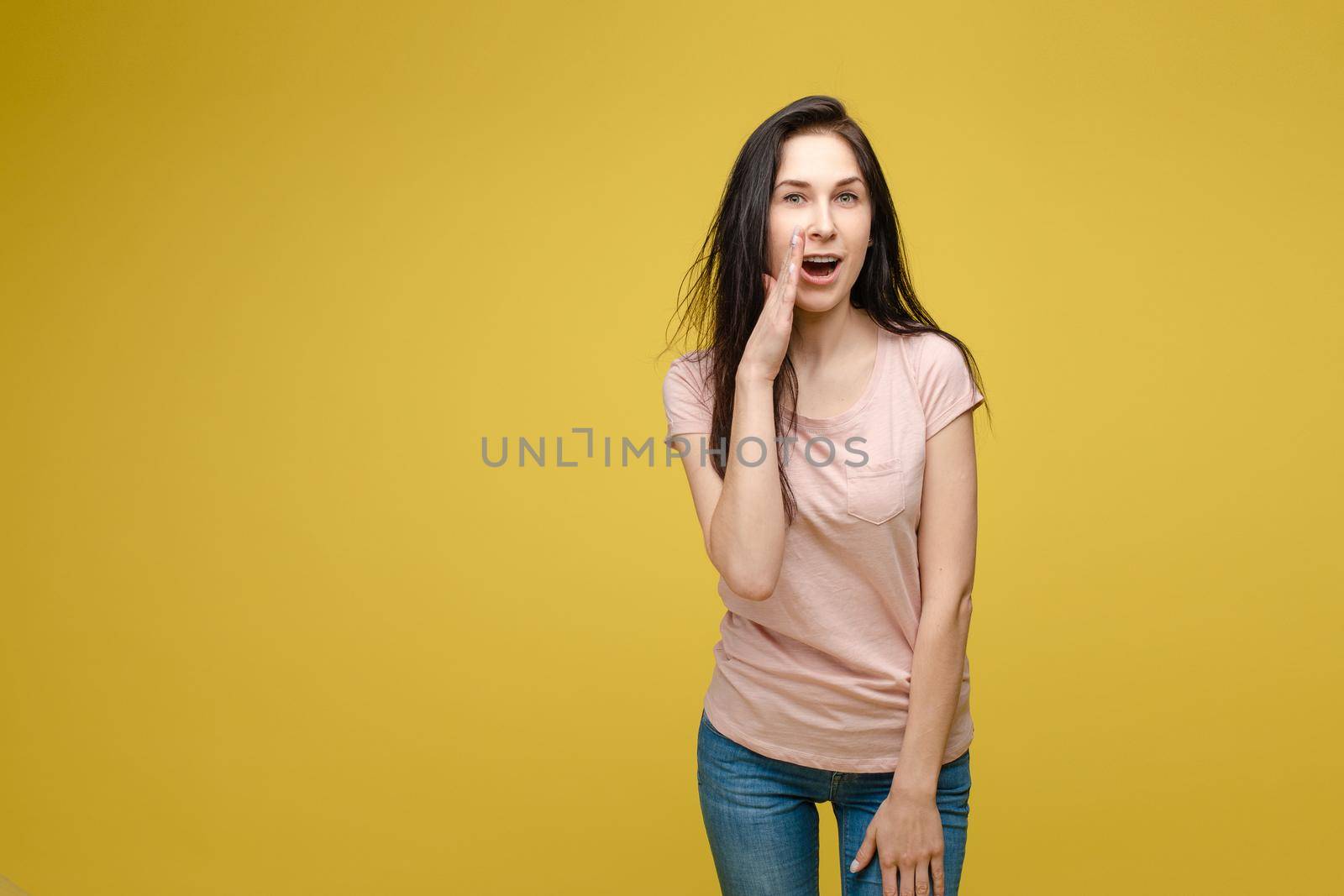 Studio portrait of curious brunette girl in multicolored top listening to the news or gossips with her ear.