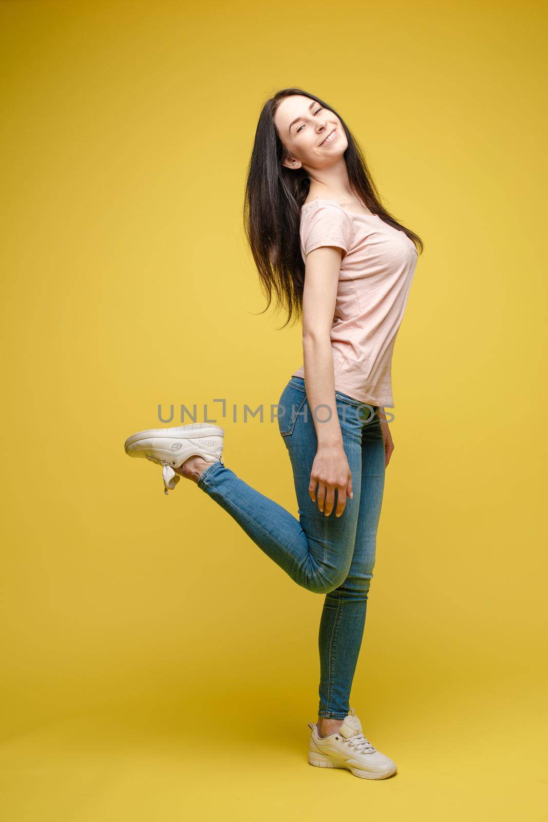 Cheerful brunette young woman in casual outlook jumping in mid air in studio. by StudioLucky