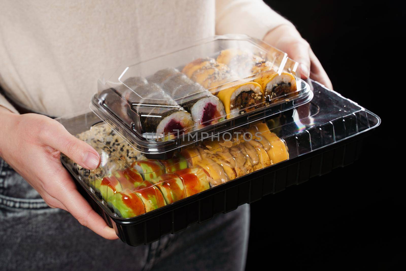 Sushi roll food delivery service. Holding sushi set box on black background. Traditional Japanese seafood. Delicious roll.