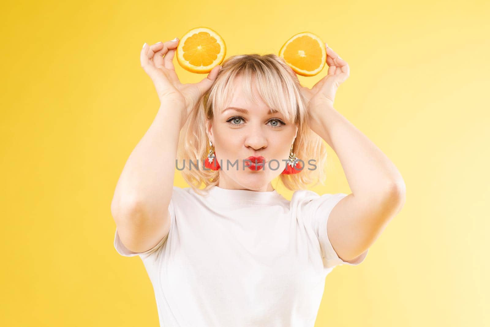 Beautiful, cheerful woman playing with orange slices. Orange circles. Juice ads. Perky frame. Yellow background by StudioLucky