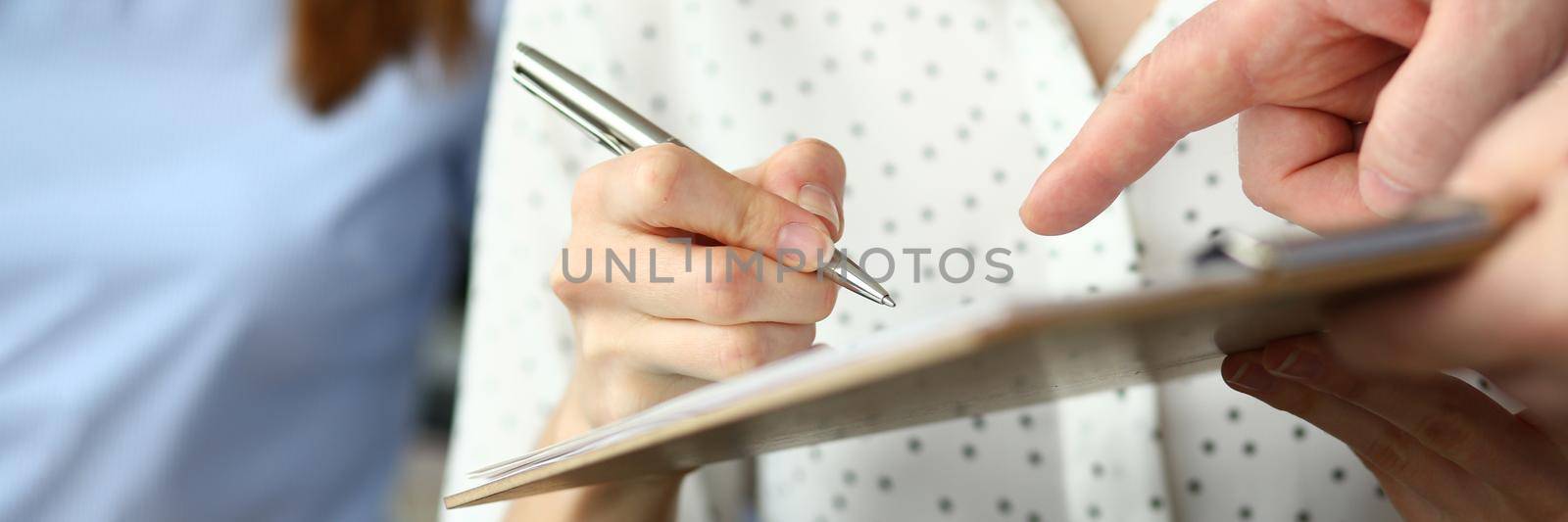 Close-up of smart people working in big modern office with smart manager. Trendy woman in classy blouse writing something in paper folder. Company meeting concept