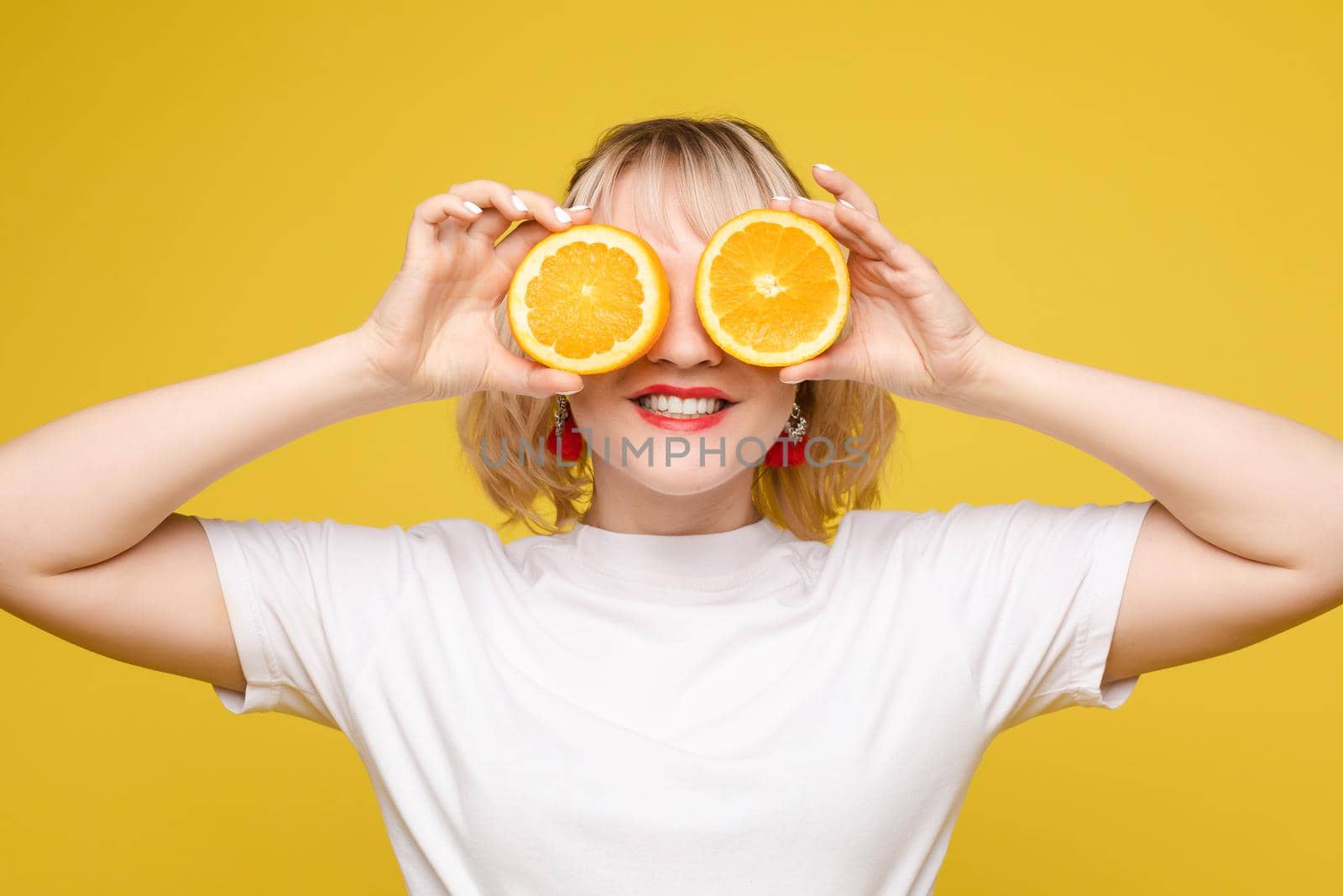 Beautiful, cheerful woman playing with orange slices. Orange circles. Juice ads. Perky frame. Yellow background by StudioLucky