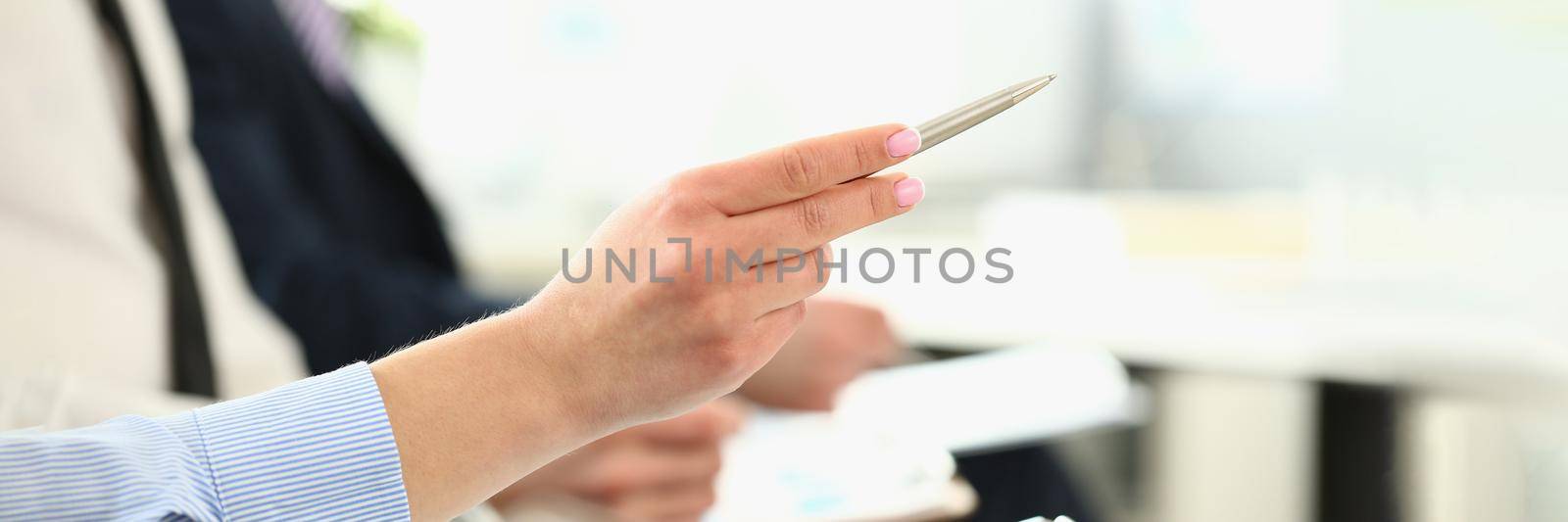 Focus on friendly colleagues discussing new business project. Gorgeous woman with pen pointing with writing utensil in big modern office building. Company meeting concept. Blurred background