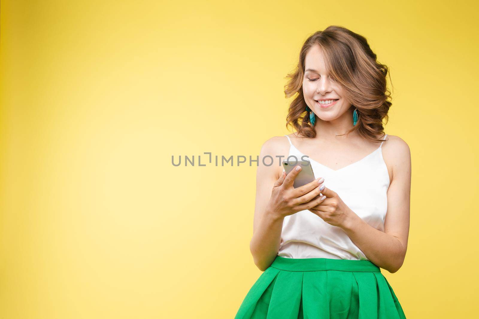 Studio portrait of beautiful caucasian brunette woman in patterned overall pointing at her smartphone with index finger. She is certain or sure about something. I know gesture.