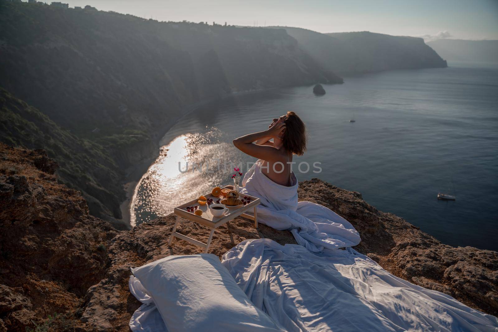Woman wake up in bed wuth duvet and pillow over nature sea background outdoors. Back view. Good morning. Freedom concept
