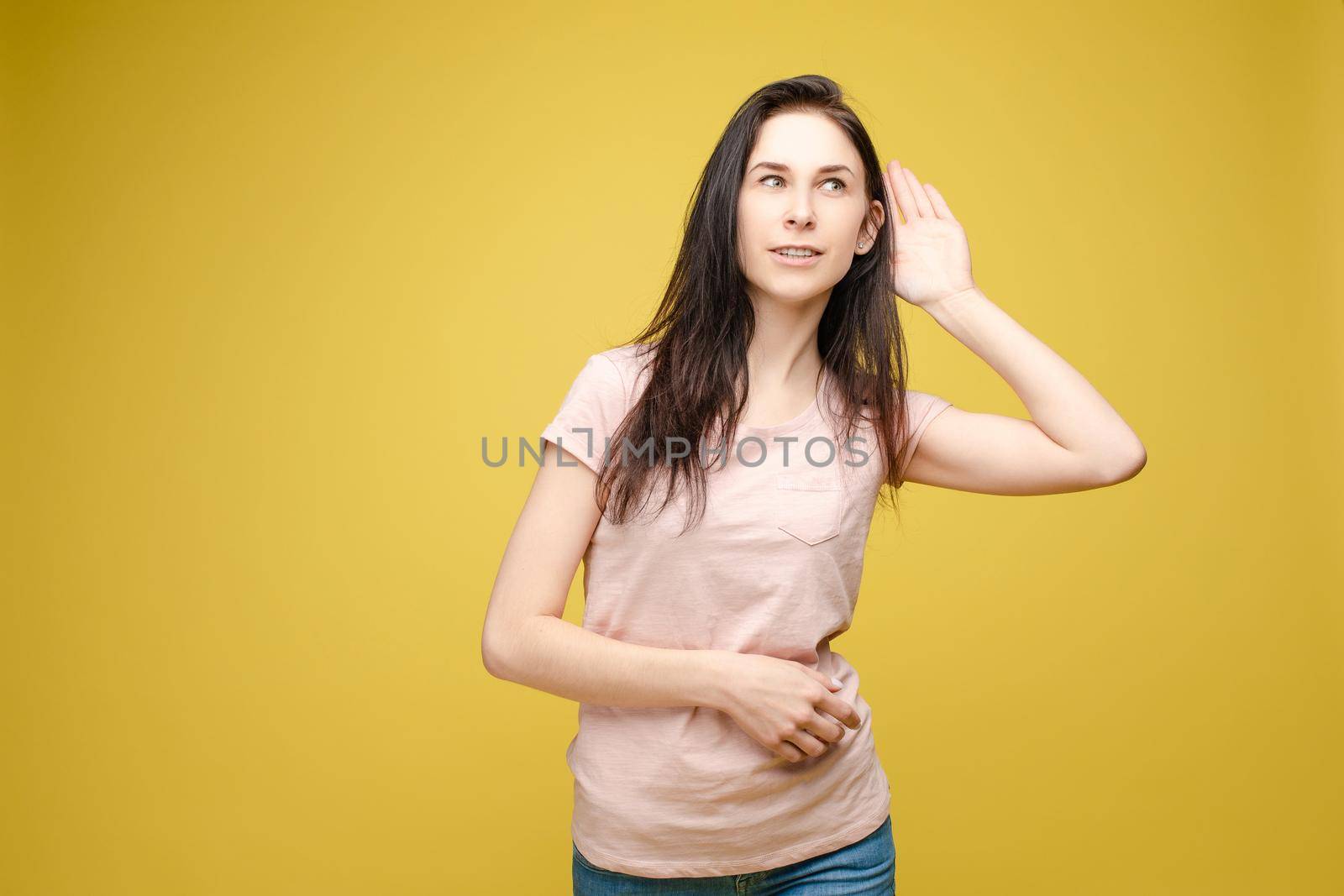 Studio portrait of curious brunette girl in multicolored top listening to the news or gossips with her ear.