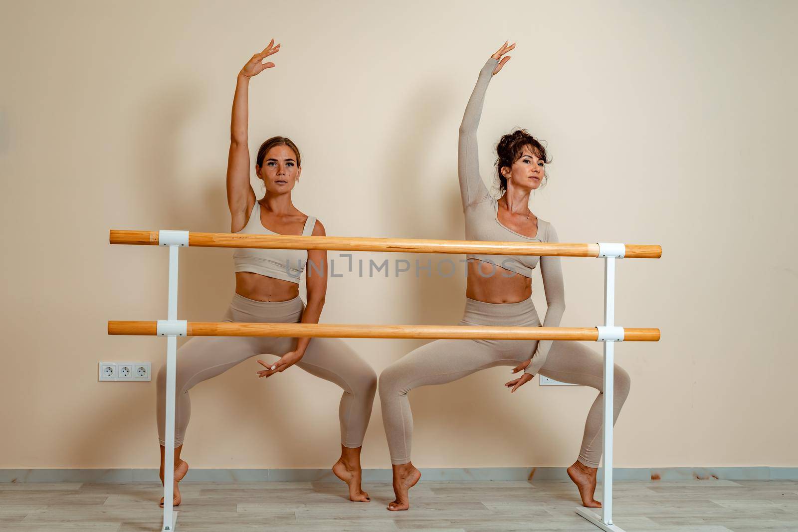 Near the barre, in the choreographic hall, two women in a beige top and leggings are engaged