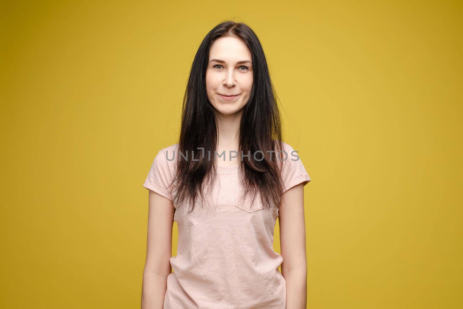 Pretty blonde haired woman wearing in black sweater, holding messy unbrushed hair in one hand and pink hairbrush in another one. A frustrated girl looks at her hair on a white studio background.