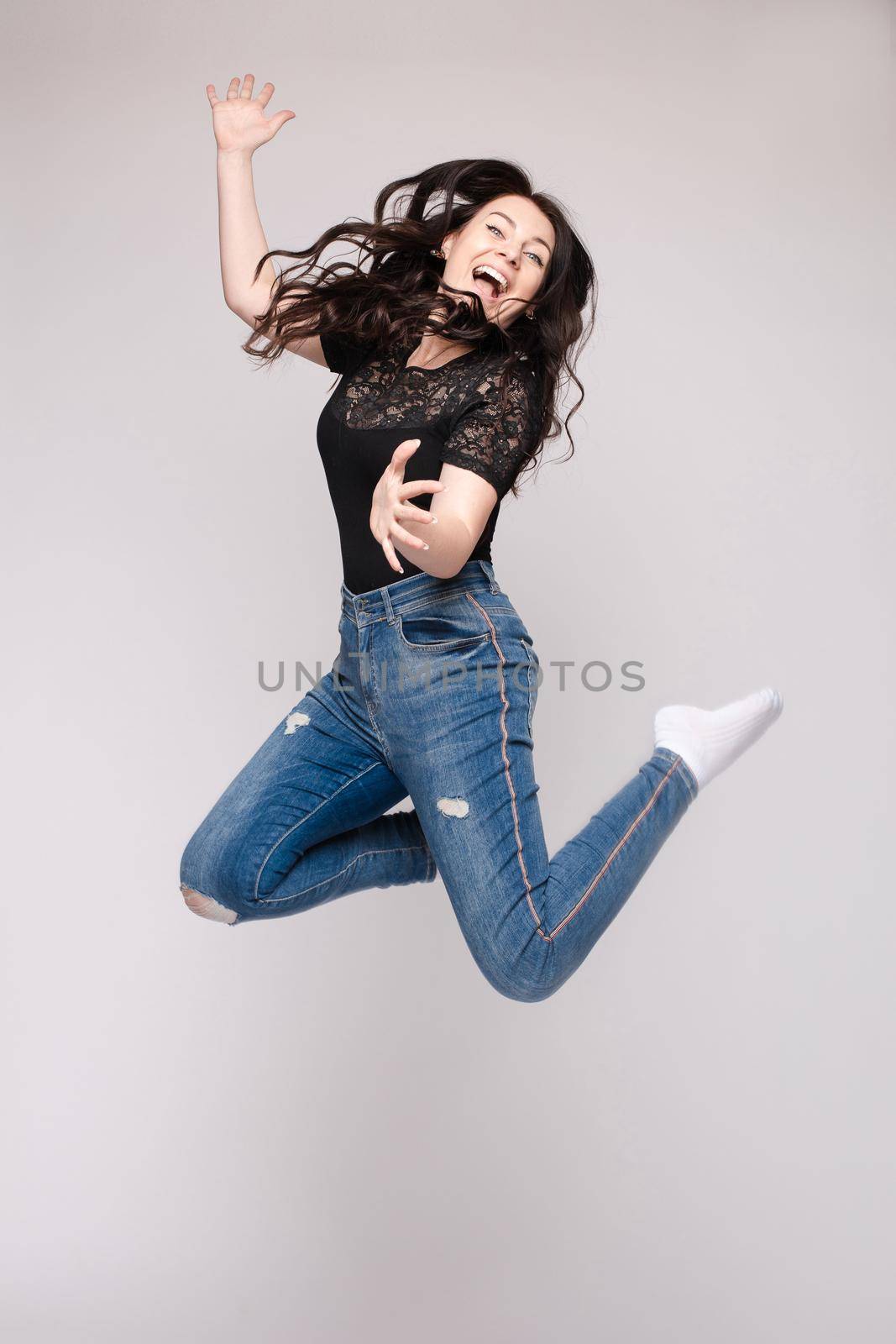 Full length isolate portrait of positive brunette young girl in jeans and t-shirt and sneakers jumping over yellow background. She is smiling at camera.