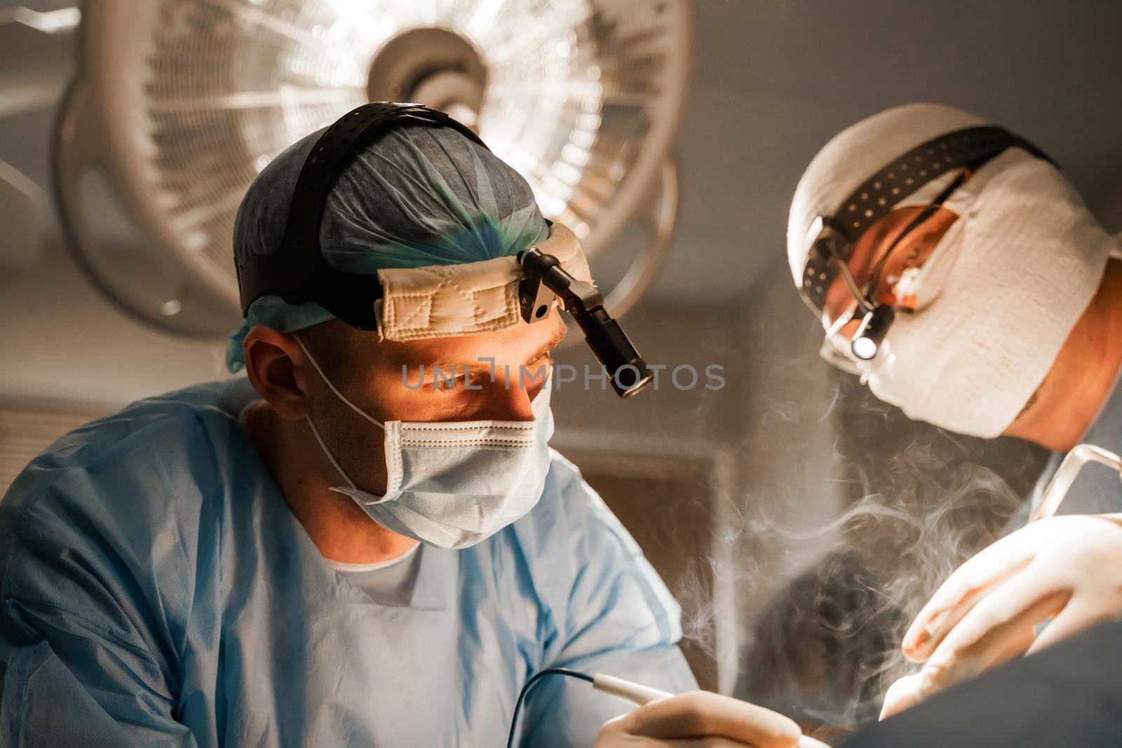 2 surgeons with headlamp do plastic operation in medical clinic. Chest augmentation plastic operation and correction in medical clinic