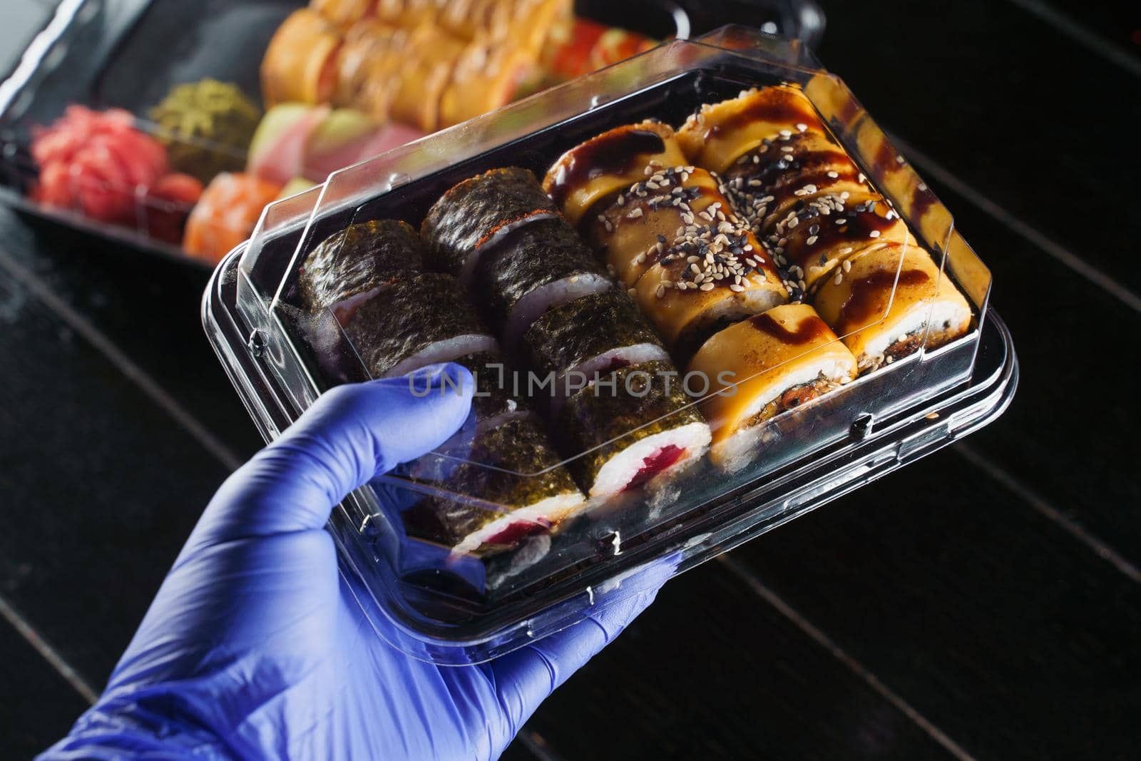 Sushi roll food delivery service at quarantine covid-19 period. Holding sushi set box using medical gloves on black background