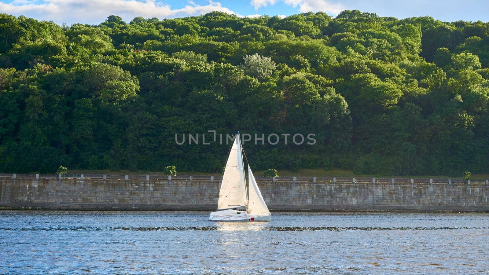 a medium-sized sailboat equipped for cruising or racing.Small yacht on the background of the coast with a stone wall and forest.