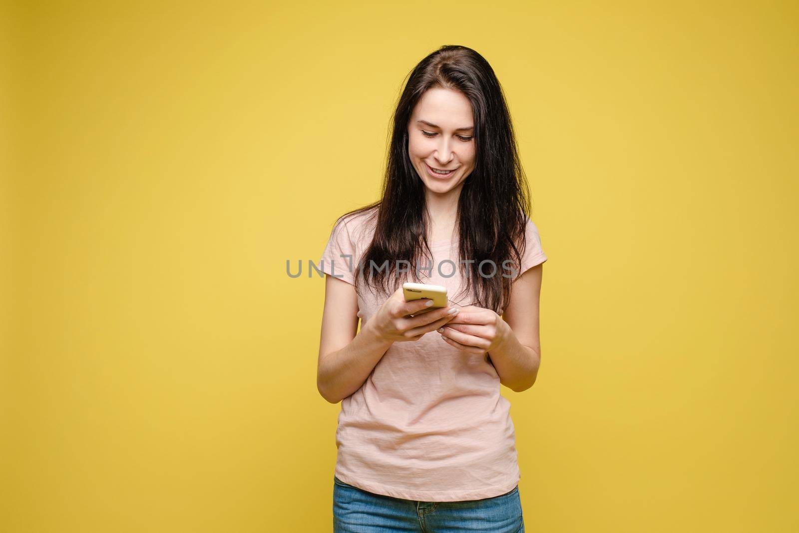 Studio portrait of beautiful caucasian brunette woman in patterned overall pointing at her smartphone with index finger. She is certain or sure about something. I know gesture.