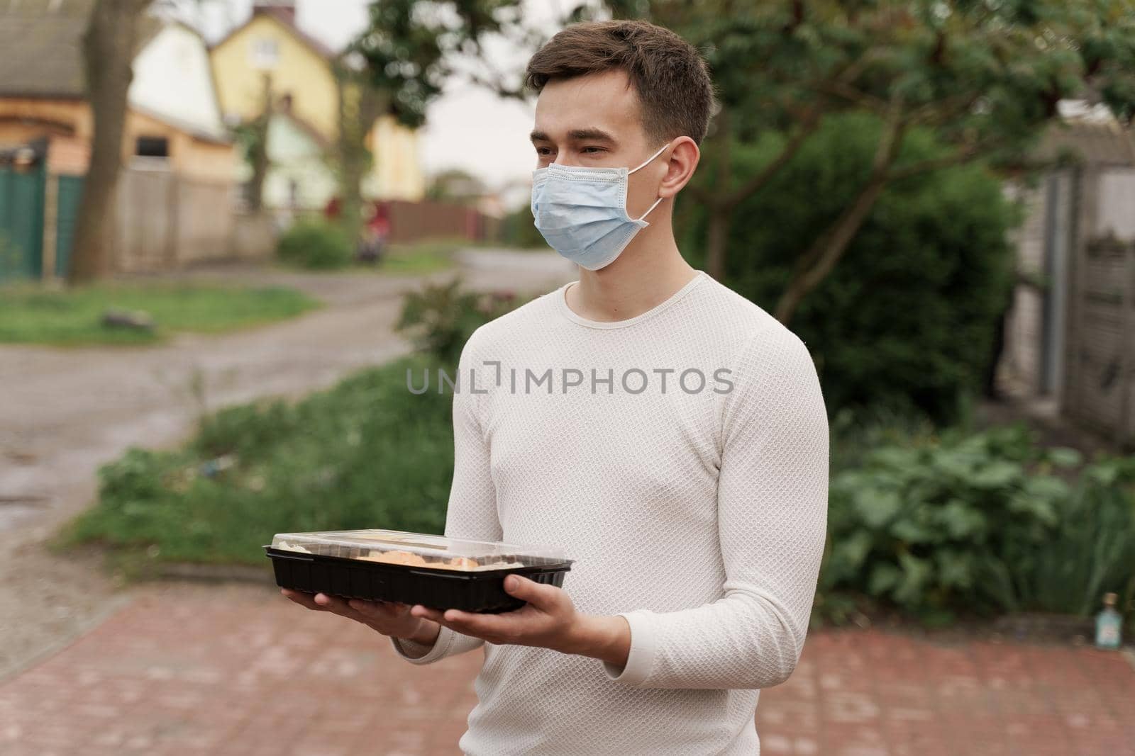 Sushi set in box healthy food delivery online service by car. Man courier in medical mask with sushi box stands in front of car