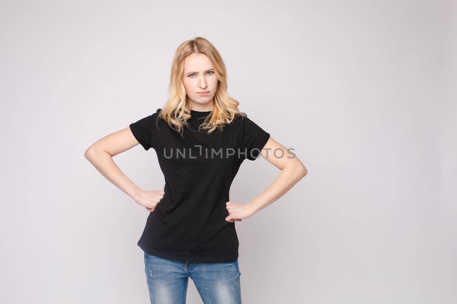 Studio portrait of unsatisfied young brunette caucasian woman with wavy hair in overall with colorful pattern holding arms folded and looking at camera with grief, dissatisfaction, anger and disbelief. Isolate.