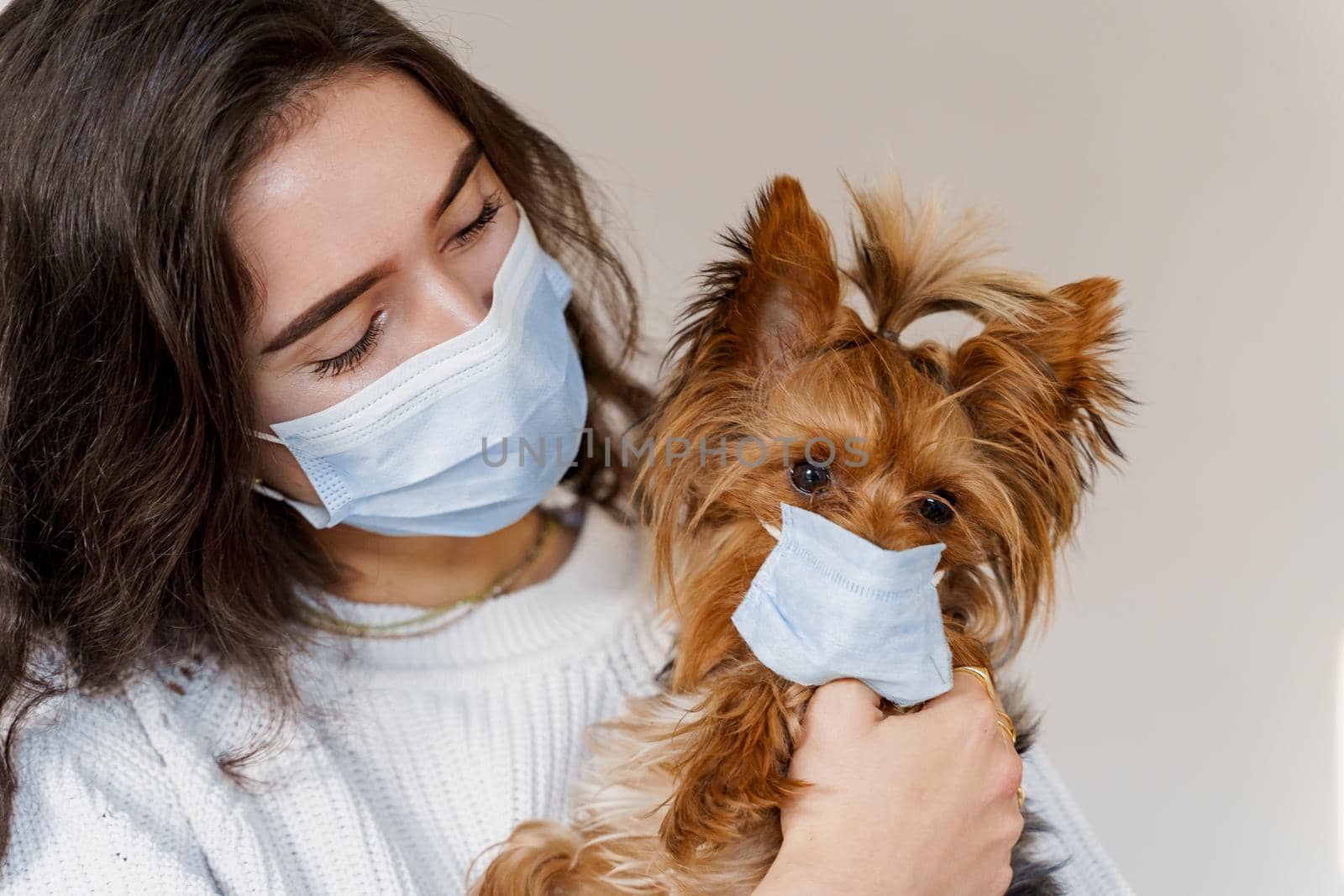 Young woman in medical mask hugs her dog yorkshire terrier wearing protective mask too
