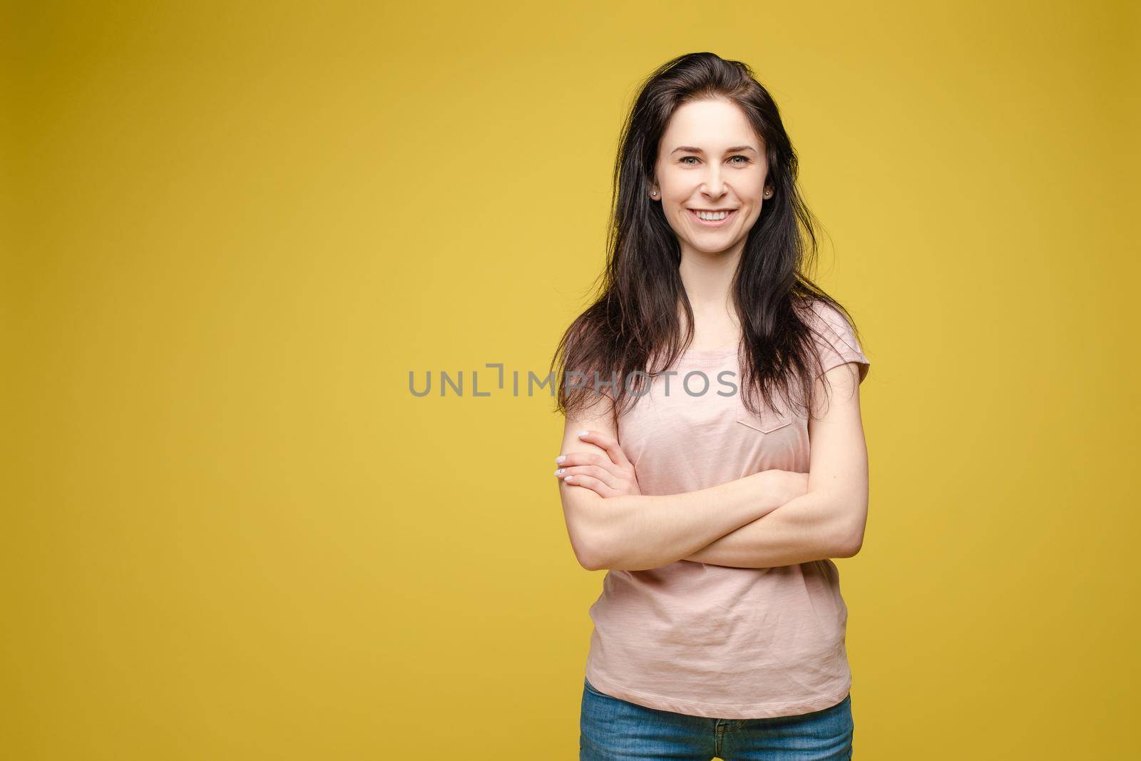 Studio portrait of fashionable brunette lady in white dress with flowers and beige heels posing with bent leg. Smiling at camera. holding skirt. Isolate on yellow background.