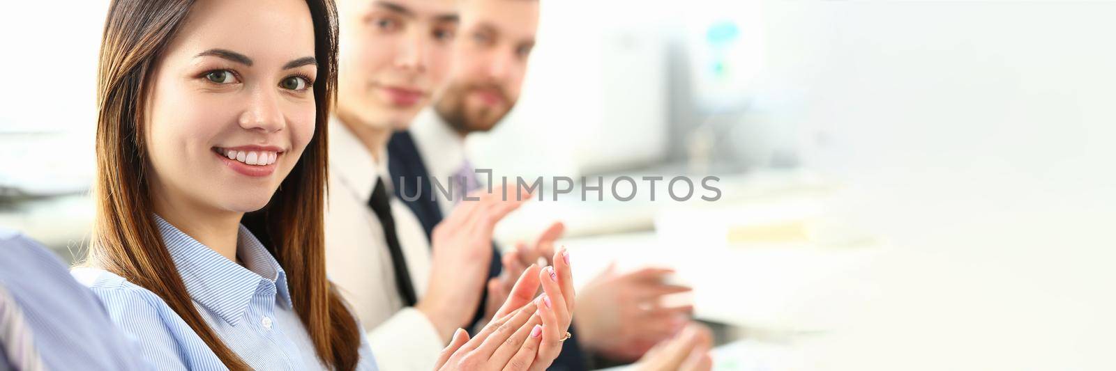 Portrait of attractive woman looking at camera with great joy and calmness. Gorgeous female sitting among good and friendly colleagues and clap to man discussing new project. Company meeting concept
