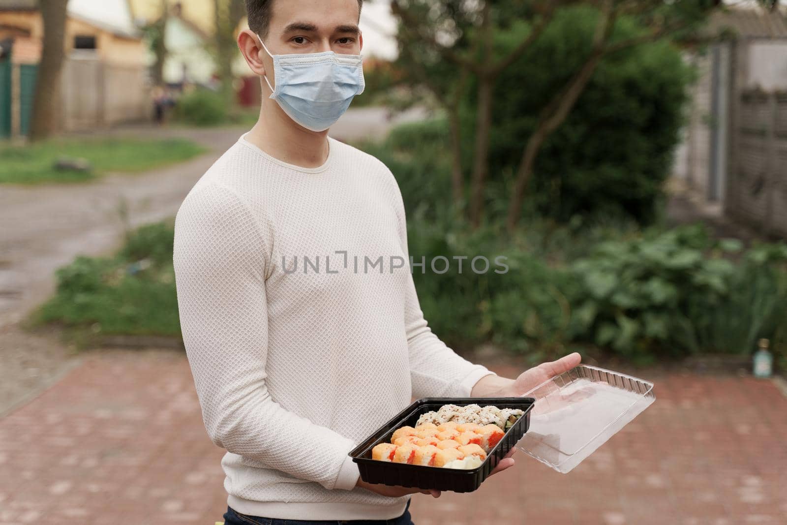 Sushi set in box healthy food delivery online service by car. Man courier in medical mask opens sushi box. by Rabizo