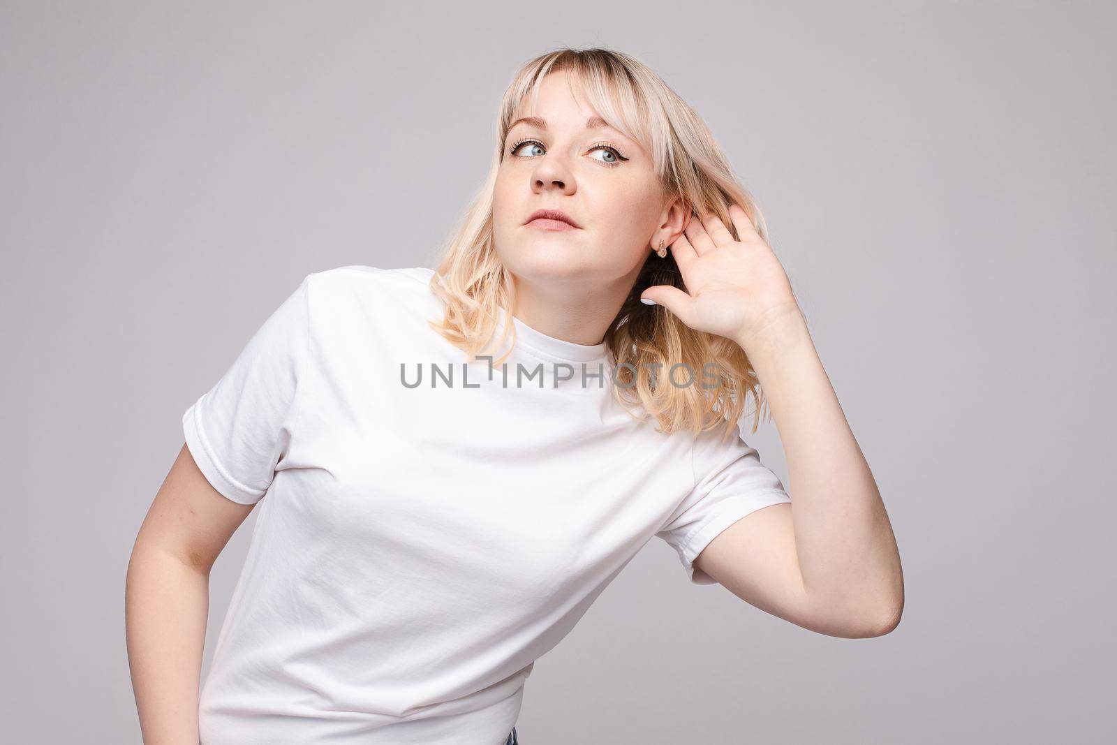 Studio portrait of curious brunette girl in multicolored top listening to the news or gossips with her ear.