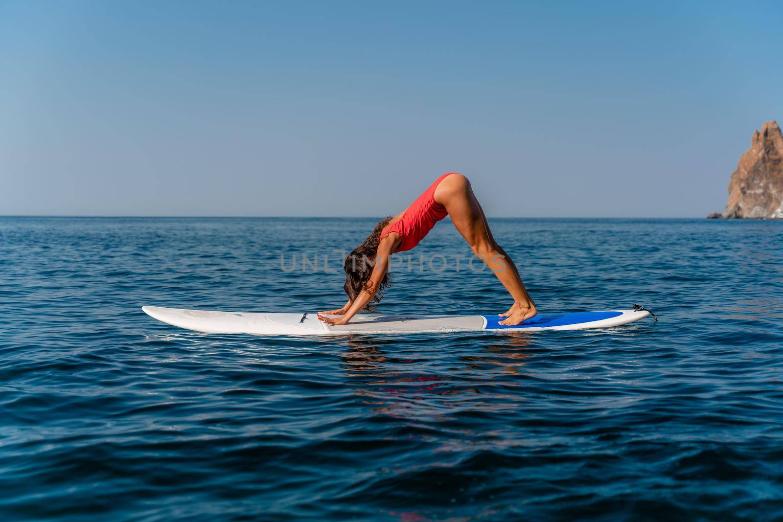 Sporty girl on a surfboard in the sea on a sunny summer day. In a red swimsuit, she sits in the splits on the sap. Summer entertainment on Stortom by the sea by Matiunina