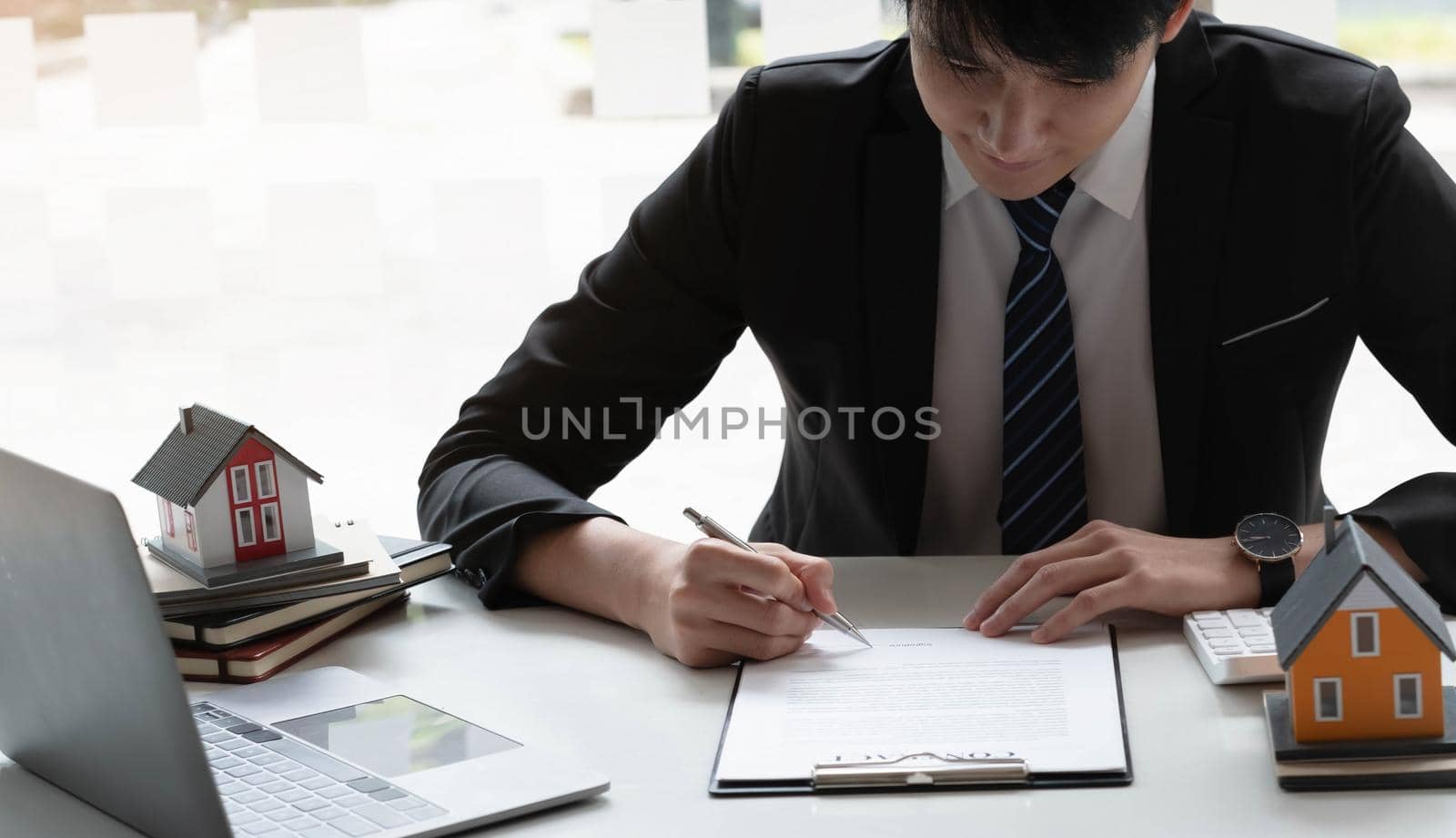 Real estate agent with house model hand putting signing contract,have a contract in place to protect it,signing of modest agreements form in office.Concept real estate,moving home or renting property by wichayada