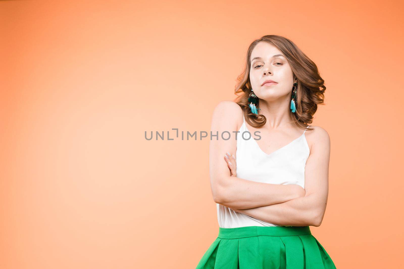 Studio portrait of unsatisfied young brunette caucasian woman with wavy hair in overall with colorful pattern holding arms folded and looking at camera with grief, dissatisfaction, anger and disbelief. Isolate.