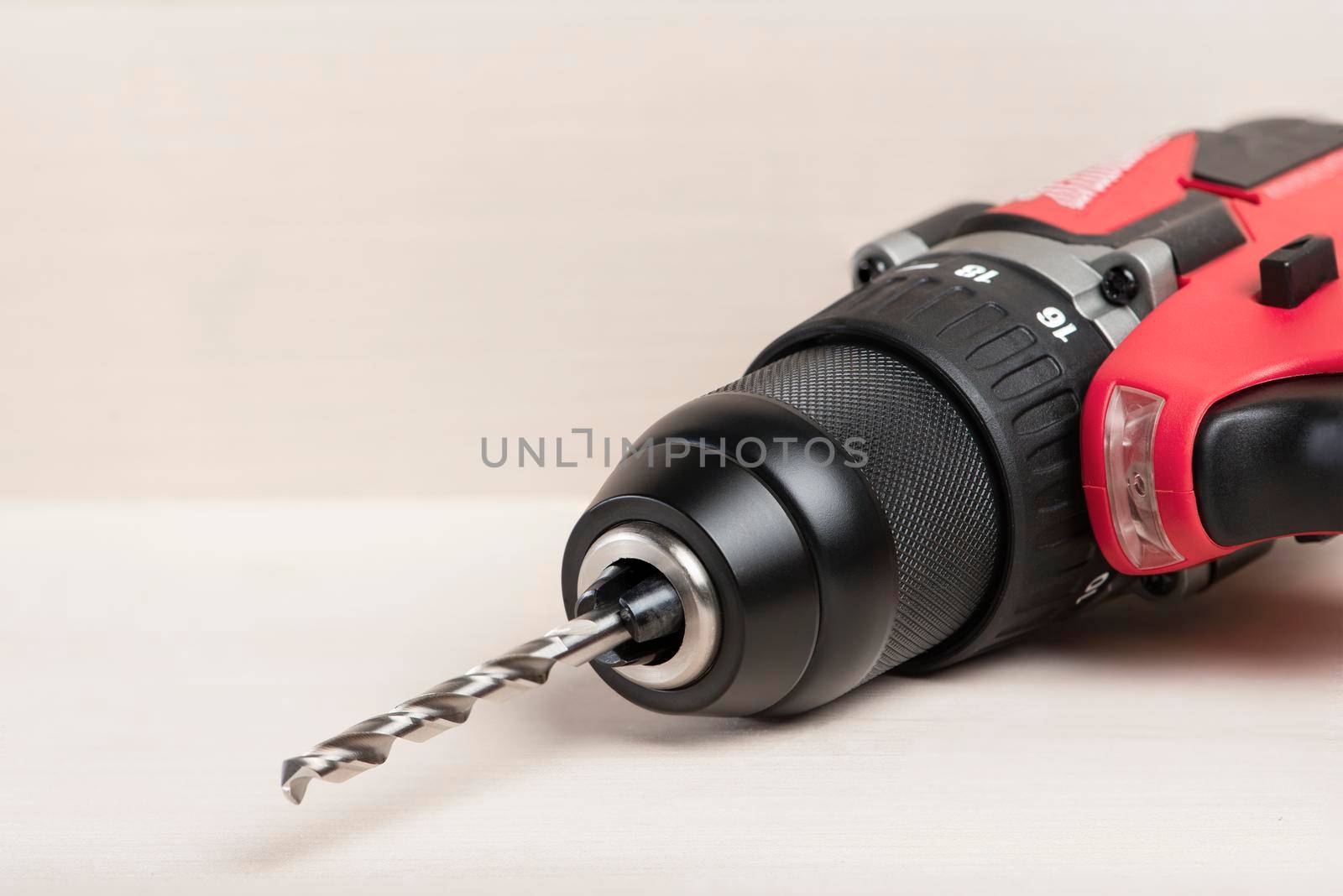 Cordless drill in black and red. A screwdriver with a drill lies on a wooden background. Modern carpentry tool close-up