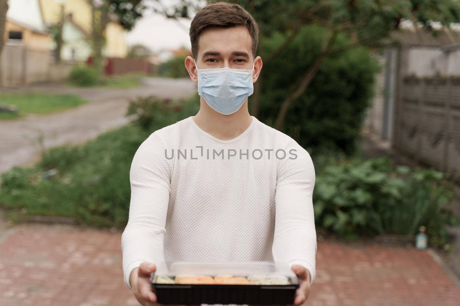 Sushi set in box healthy food delivery online service by car. Handsome man courier in medical mask gives sushi box to you. Japanese cuisine