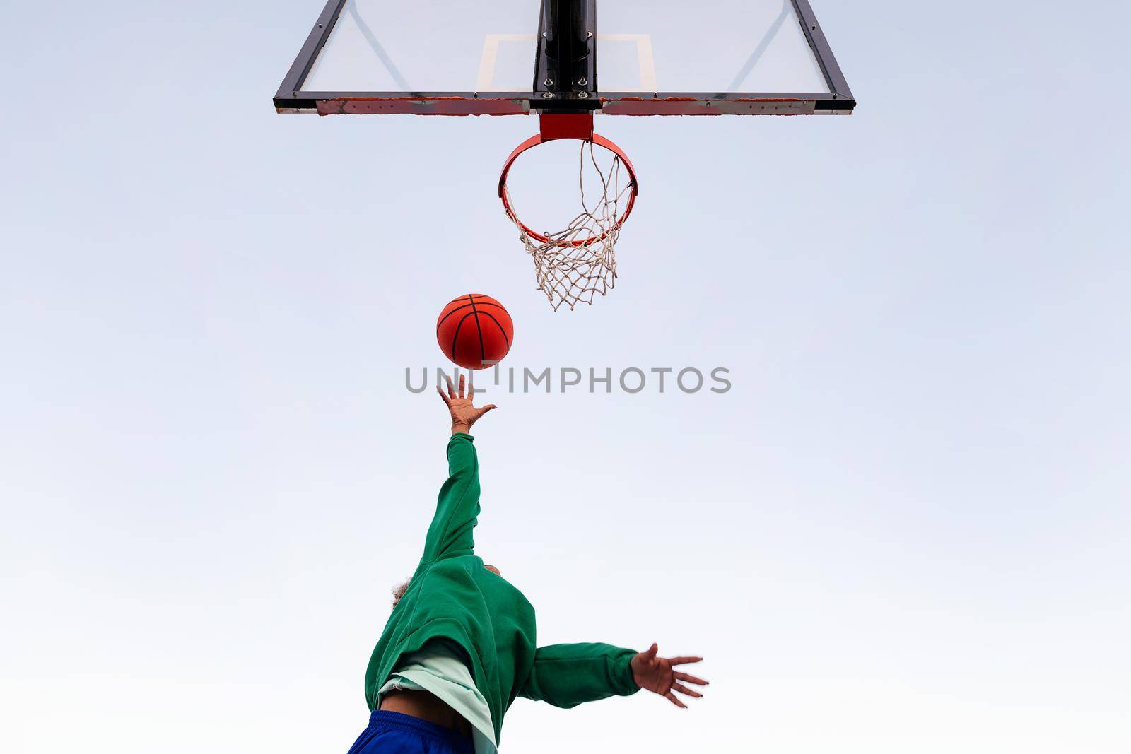 unrecognizable latin woman shooting in a basketball hoop seen from below with the sky in the background, concept of urban sport outdoors, copy space for text