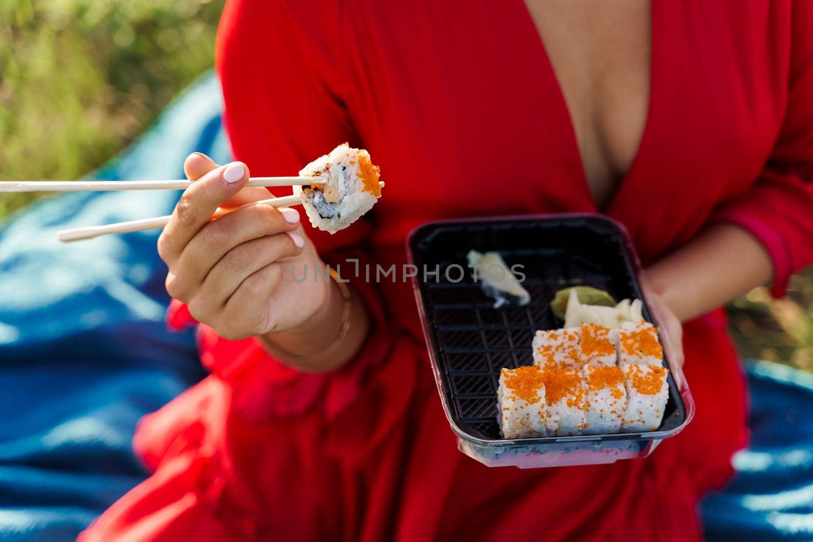Close-up sushi set food delivery. Sexy girl holds sushi with chopsticks in hands. Courier delivered sushi set for pretty woman. Black box with sushi, wasabi, ginger.
