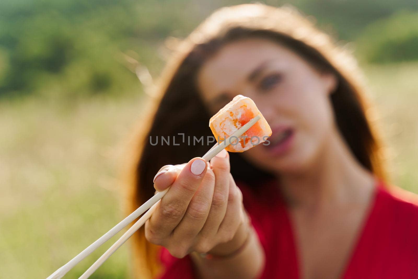 Close-up one sushi. Attractive girl holds sushi with chopsticks in hands and gives to you. Courier delivered sushi set for pretty woman. Black box with sushi, wasabi, ginger.
