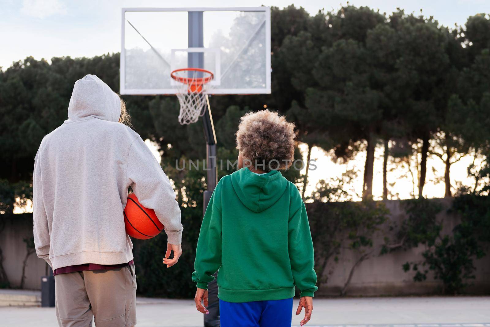 rear view of two friends walking on the basketball court after a game, concept of friendship and urban sport in the street, copy space for text