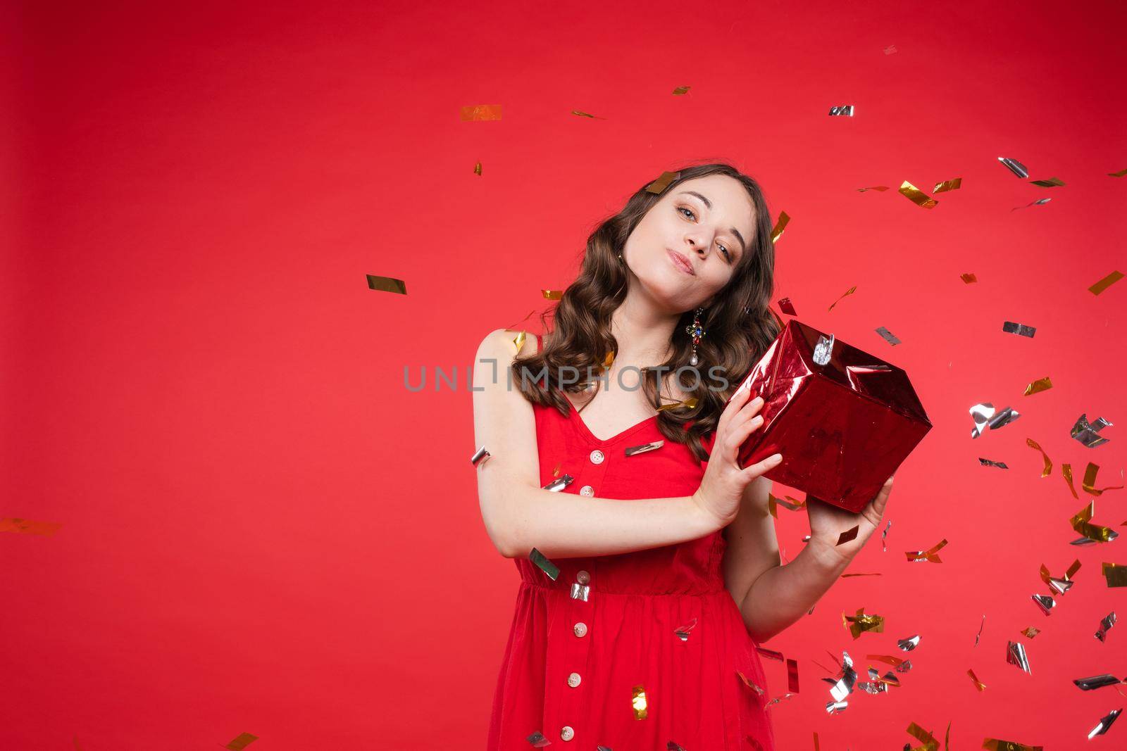 Portrait of adorable smiling young woman with long curly hair posing at red studio background by StudioLucky