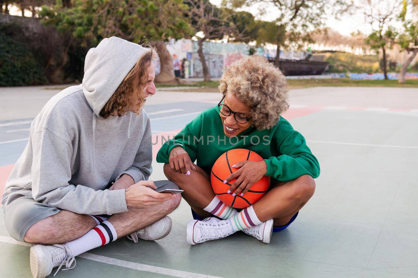 man and woman rest and have fun looking at the phone after basketball practice in a city park, concept of friendship and urban sport in the street, copy space for text