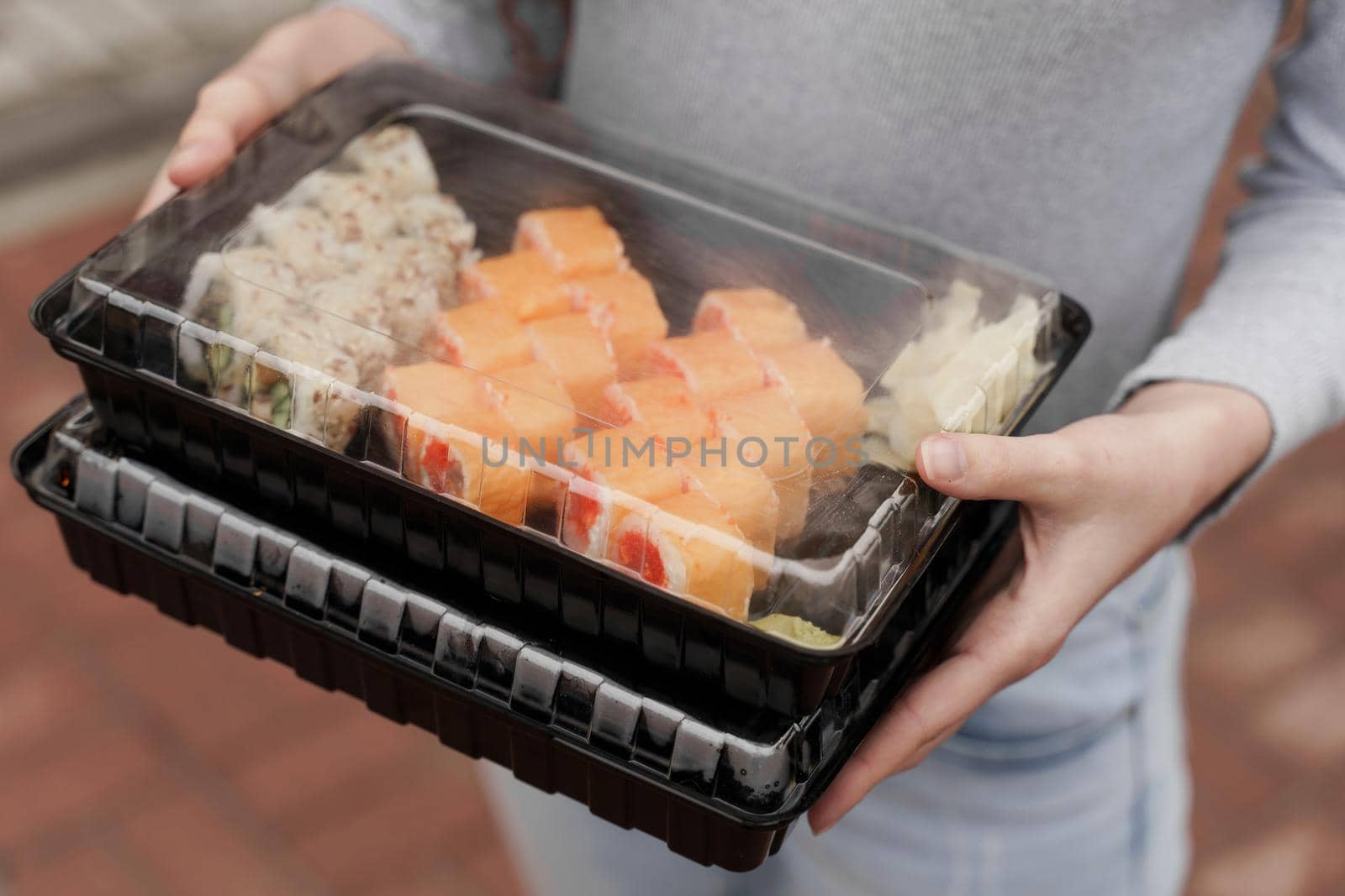 Closeup sushi set in box healthy food delivery online service. Girl holds 2 sushi sets in hands. Japanese cuisine: rolls, soy sauce, wasabi.