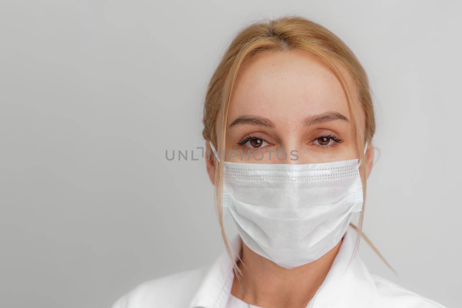 Close-up portrait of a young blonde woman in a medical mask on a light background. Virus protection. Coronovirus covid-19 The concept of a pandemic epidemic. Quarantine. Stay at home. by Matiunina