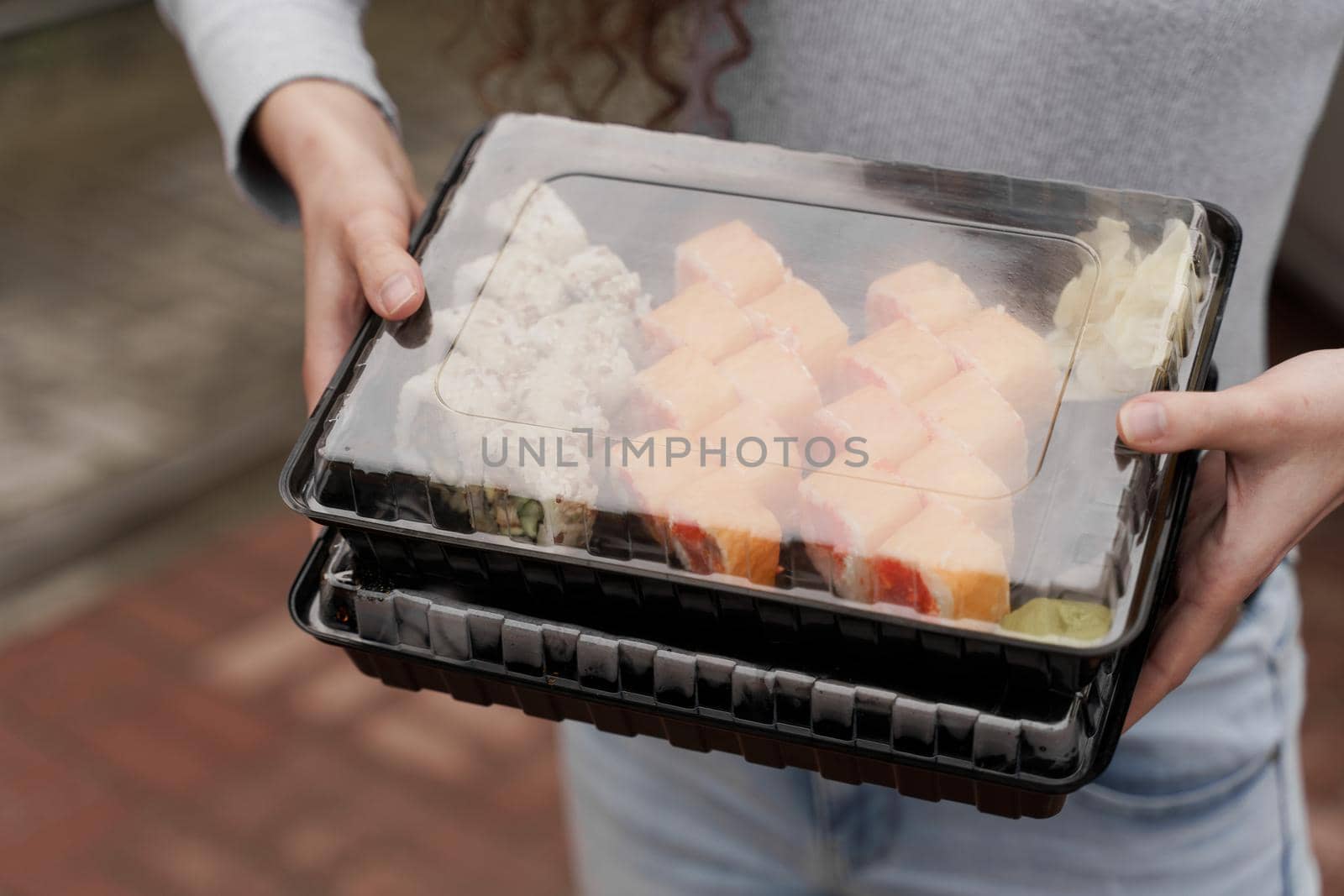 Close-up sushi in box healthy food delivery online service. Girl holds 2 sushi sets in hands. Japanese cuisine: rolls, soy sauce, wasabi.