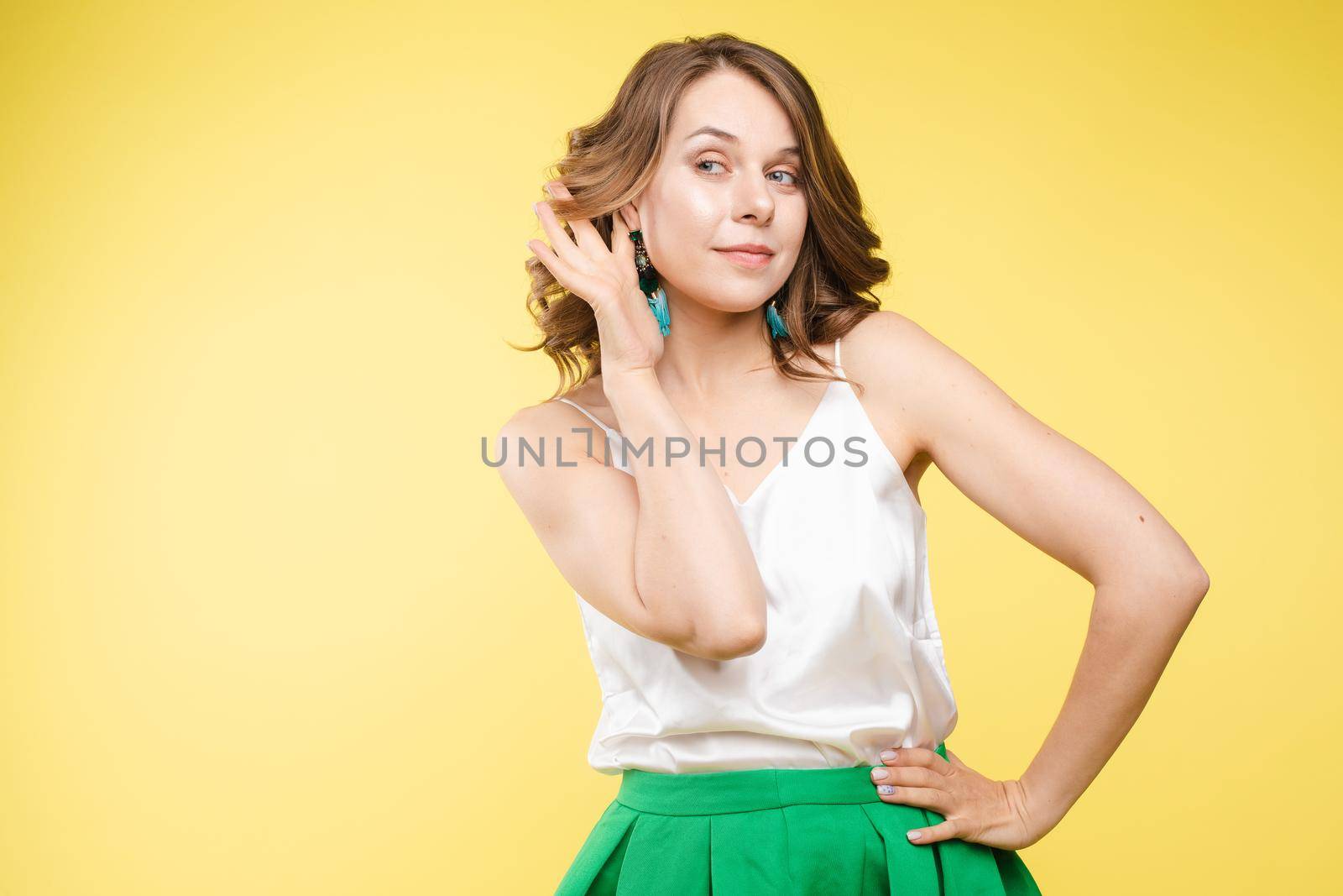 Studio portrait of curious brunette girl in multicolored top listening to the news or gossips with her ear.