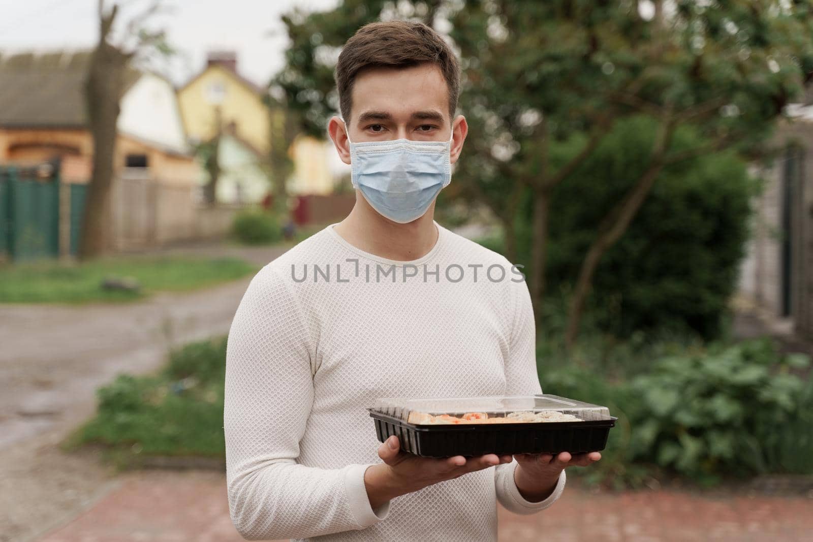 Sushi set in box healthy food delivery online service by car. Man courier in medical mask with sushi box stands in front of car
